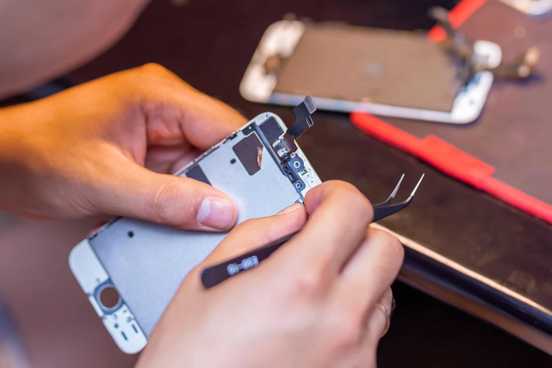 A man is repairing a mobile phone. In the frame, his hands and details of the device. repair shop for gadgets